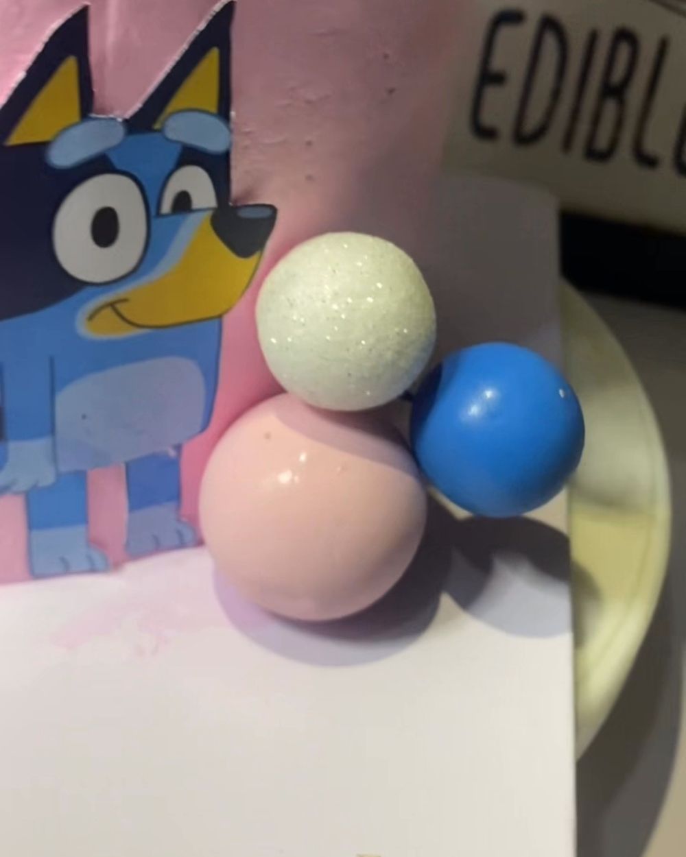 Pink kids’ cake with a Bluey cartoon topper and pastel balls